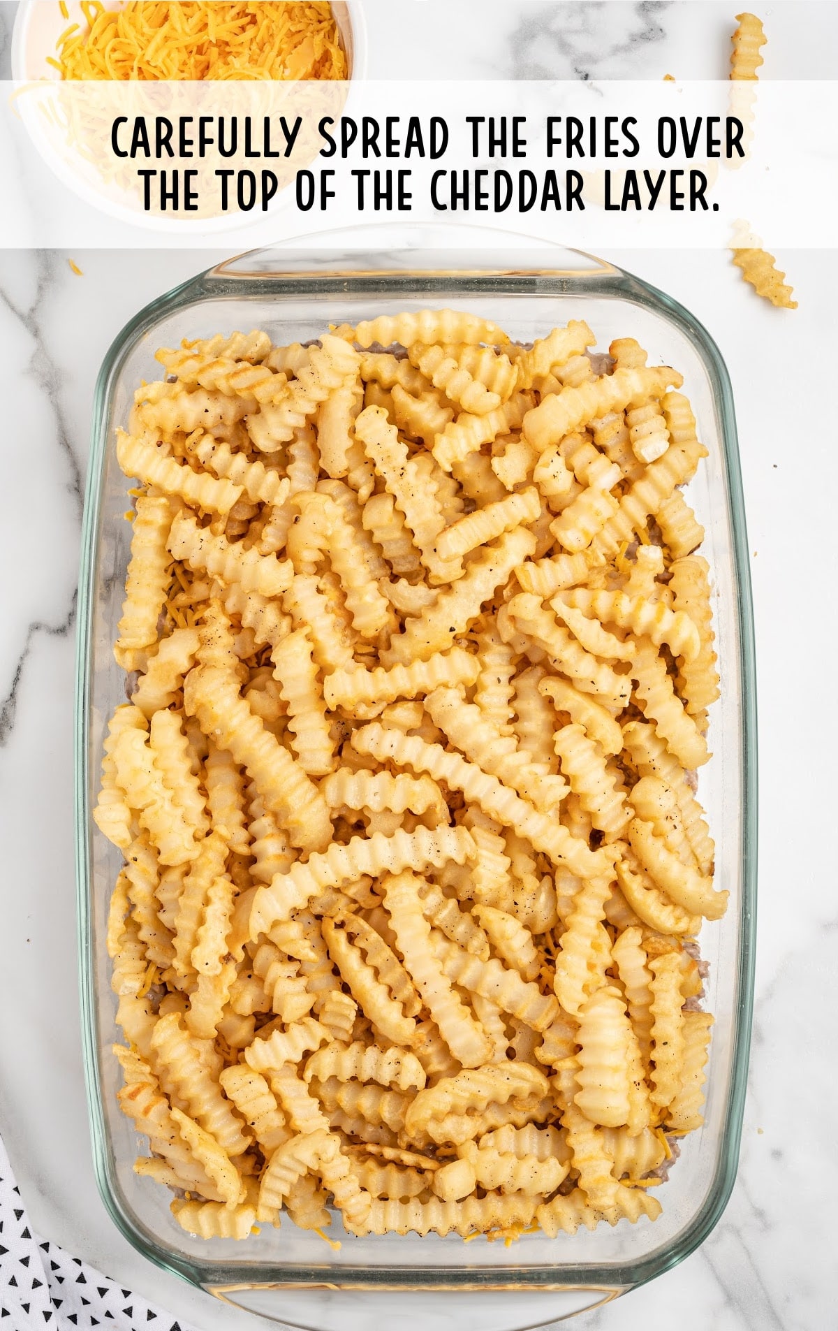 fries spread on top of the cheddar layer in a baking dish