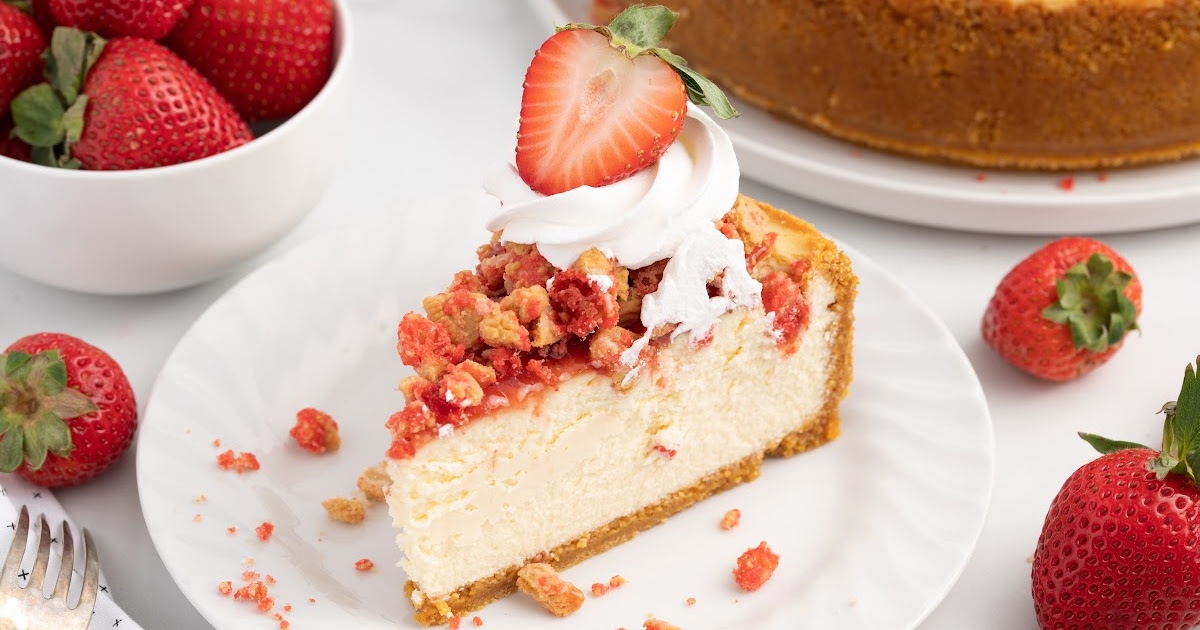 slice of strawberry crunch cheesecake on a plate topped with whipped cream and fresh strawberries