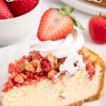 slice of strawberry crunch cheesecake on a plate topped with whipped cream and a fresh sliced strawberry