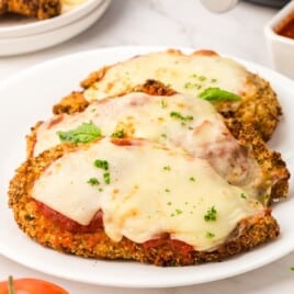 3 Pieces of cooked, cheesy chicken parmesan on a white plate.