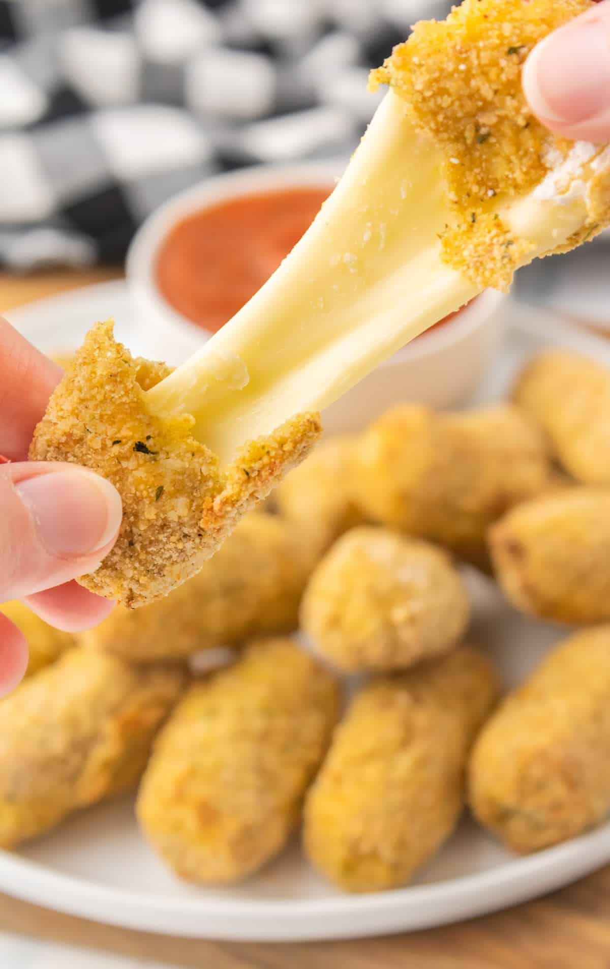 a close up shot of Air Fryer Mozzarella Sticks on a plate with one being pulled apart