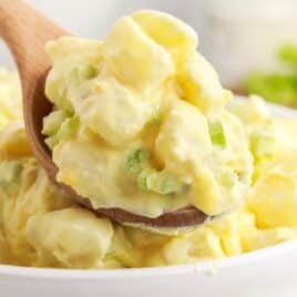 White serving bowl full of Amish potato salad with a serving spoon.