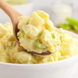 Serving spoon scooping a portion of amish potato salad out of a serving bowl.