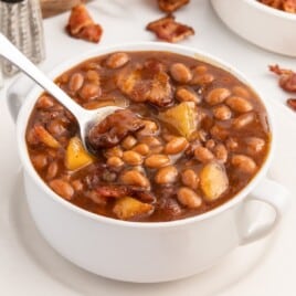 A soup bowl of apple pie baked beans with a spoon.