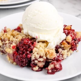 a white plate containing a serving of blackberry crumble with ice cream on top.