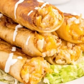 chicken flautas on a serving plate drizzled in sour cream