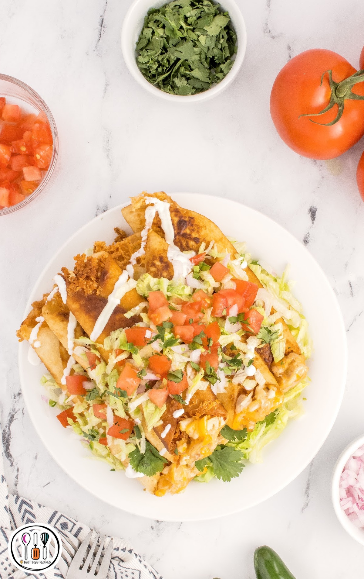 overhead shot of a plate of Chicken Flautas topped on a bead of avocado and garnished with toppings