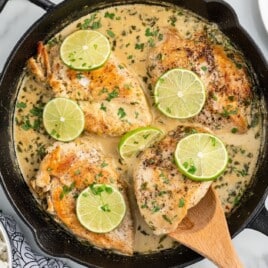 Wooden spoon lifting a piece of coconut lime chicken out of a skillet.