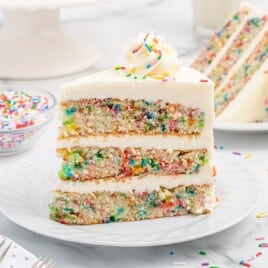 a slice of funfetti sprinkle cake is standing upright on a white plate