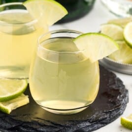 Two green tea shots garnished with limes on a black serving tray.