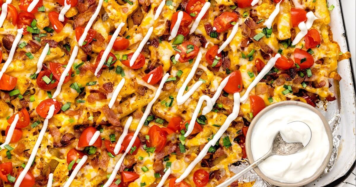 close up overhead shot of a aluminum foil of Dirty Fries topped with cheese then garnished with bacon bits and green onions