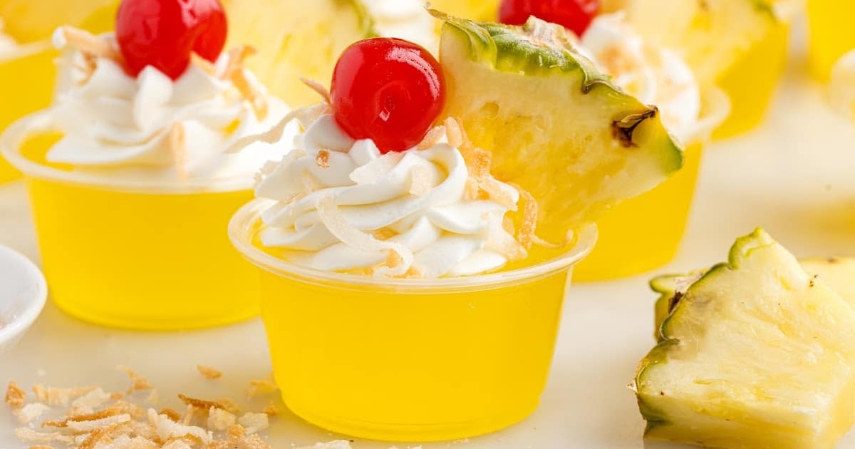 a close up shot of Pina Colada Jello Shots with one topped with a cherry and a slice of pineapple