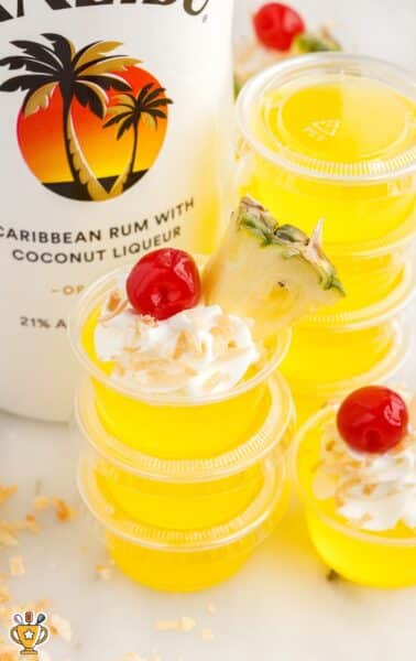 a close up shot of Pina Colada Jello Shots with one topped with a cherry and a slice of pineapple