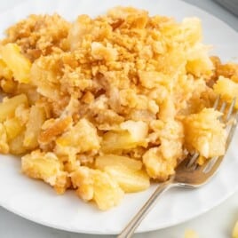 A serving of oven-baked pineapple casserole on a white plate with a fork.