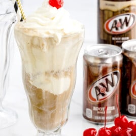 a root beer float in a float glass next to A&W root beer cans