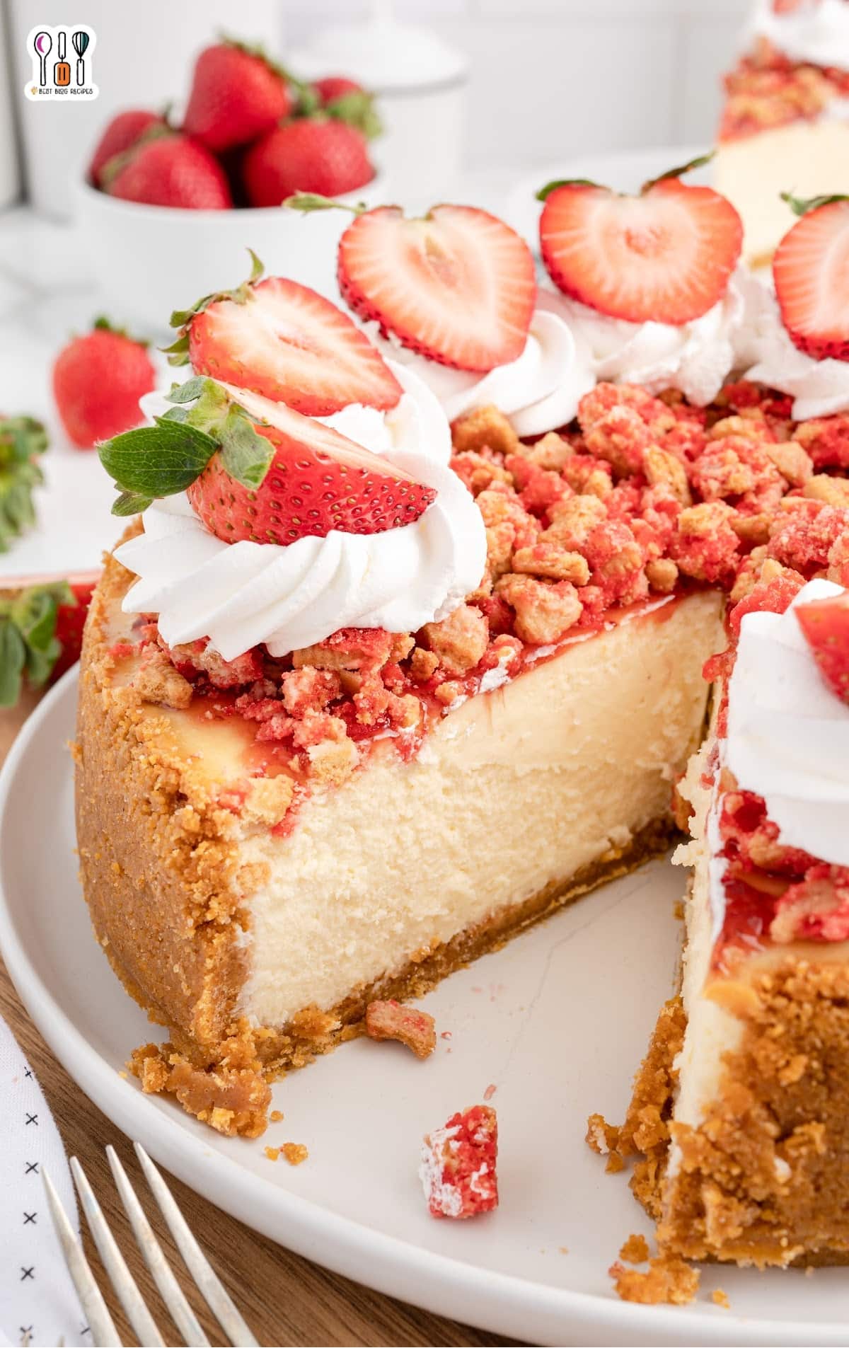 slice of strawberry crunch cheesecake on a plate topped with whipped cream and fresh strawberries