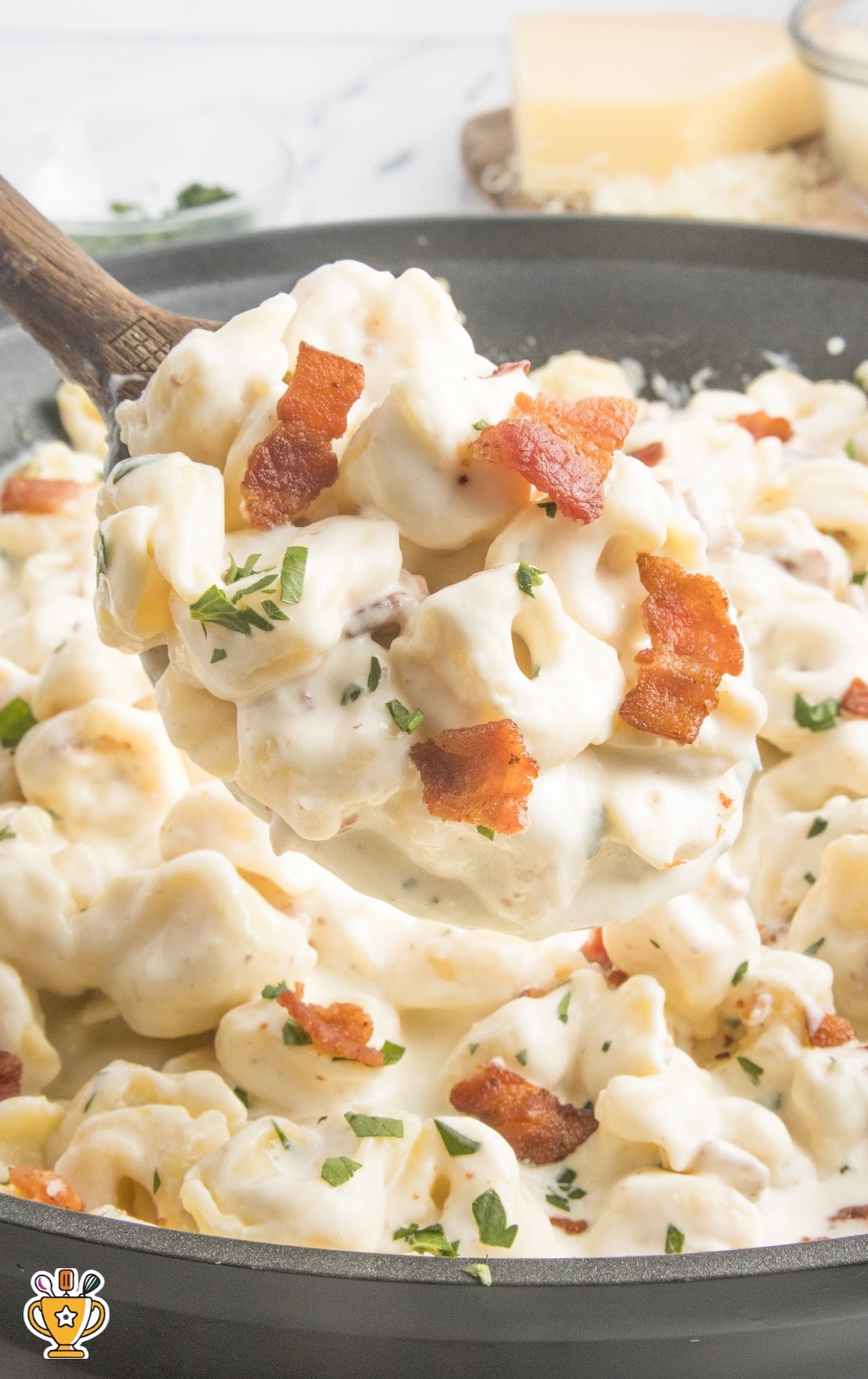 overhead shot of a wooden spoon grabbing a piece of Tortellini Carbonara