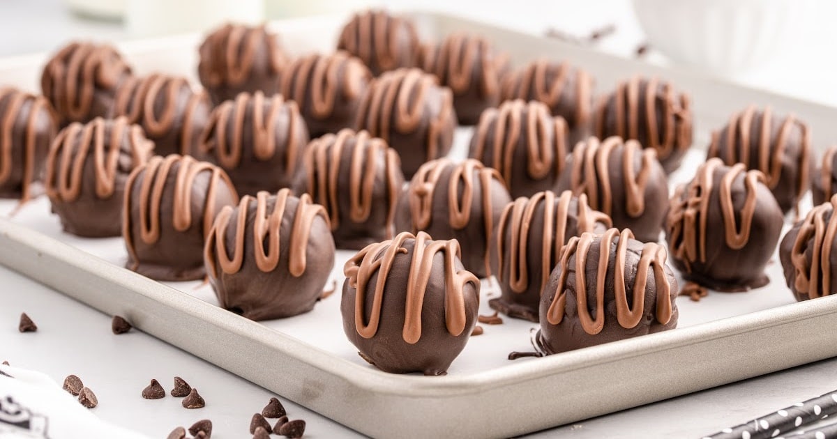 milk chocolate drizzled over the top of each cookie dough truffle on a baking sheet