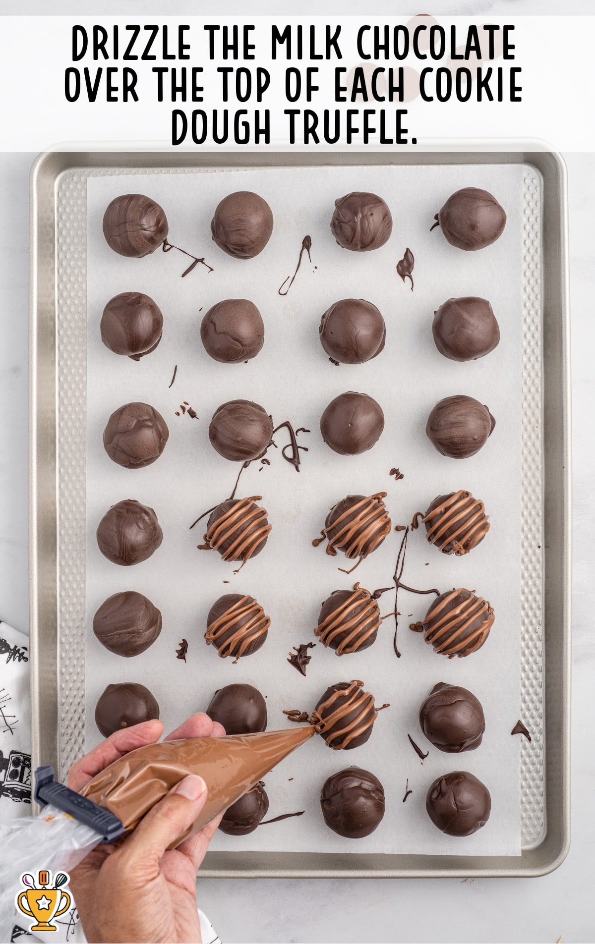 milk chocolate drizzled over the top of each cookie dough truffle on a baking sheet