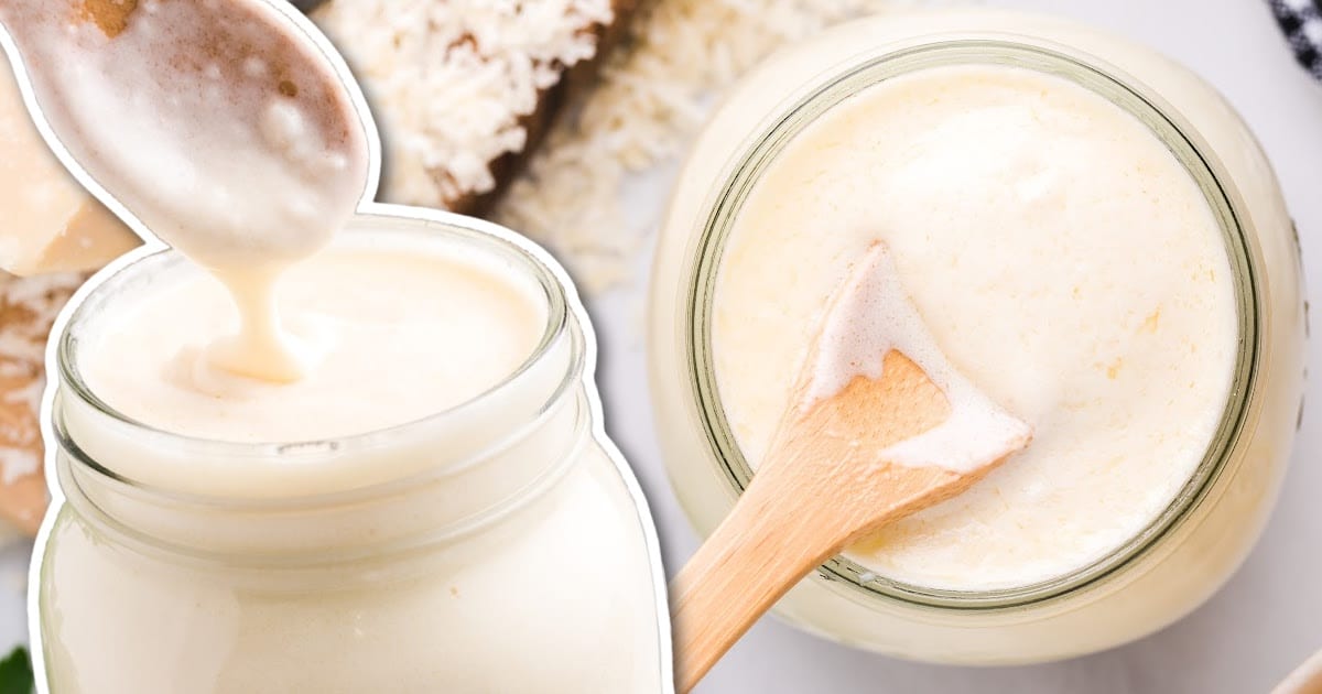 close up shot of a jar of Copycat Olive Garden Alfredo Sauce with the sauce being scooped out with a spoon