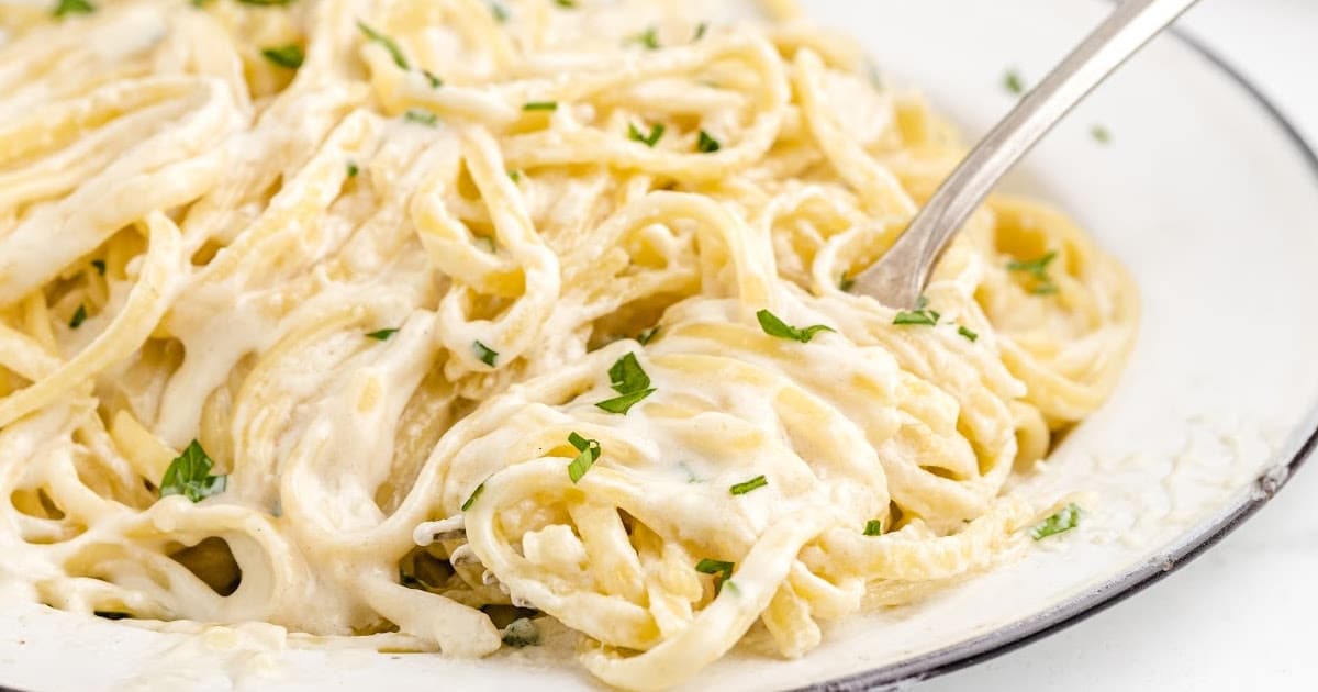 close up overhead shot of a serving of Copycat Olive Garden Alfredo Sauce with pasta and garnished with parsley in a bowl with a fork