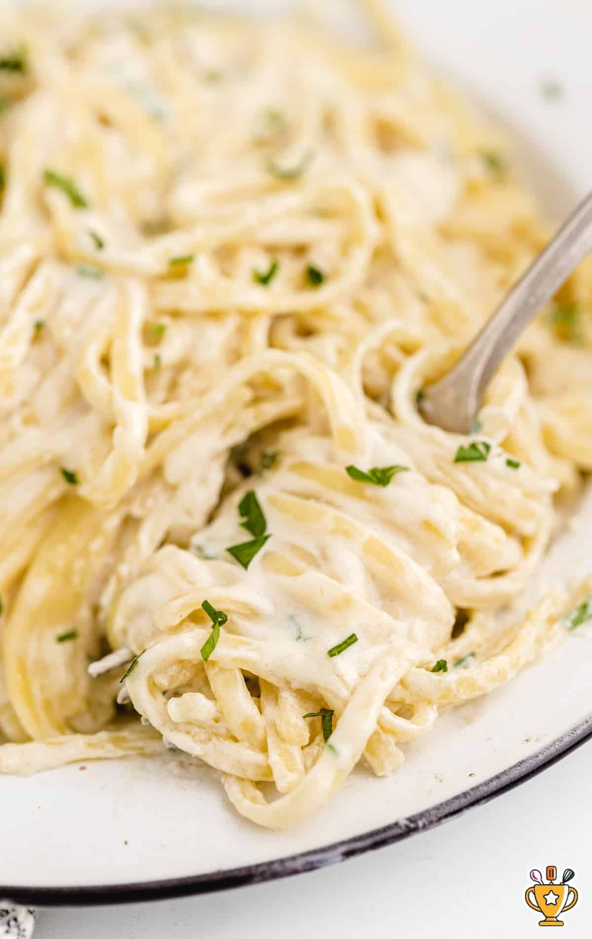 close up overhead shot of a serving of Copycat Olive Garden Alfredo Sauce with pasta and garnished with parsley in a bowl with a fork