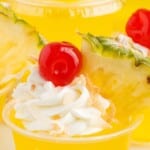 a close up shot of Pina Colada Jello Shots with one topped with a cherry and a slice of pineapple