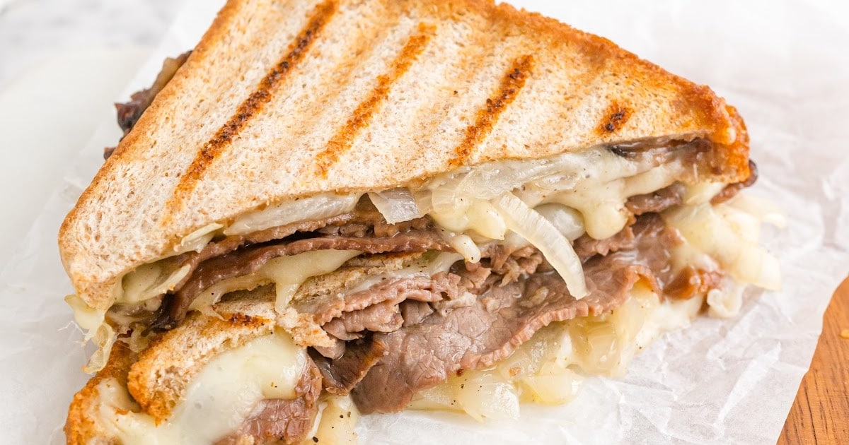 close up shot of roast beef panini with au jus cut in half and stacked on top of each other