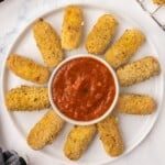 A white serving plate of mozzarella sticks and dipping sauce.