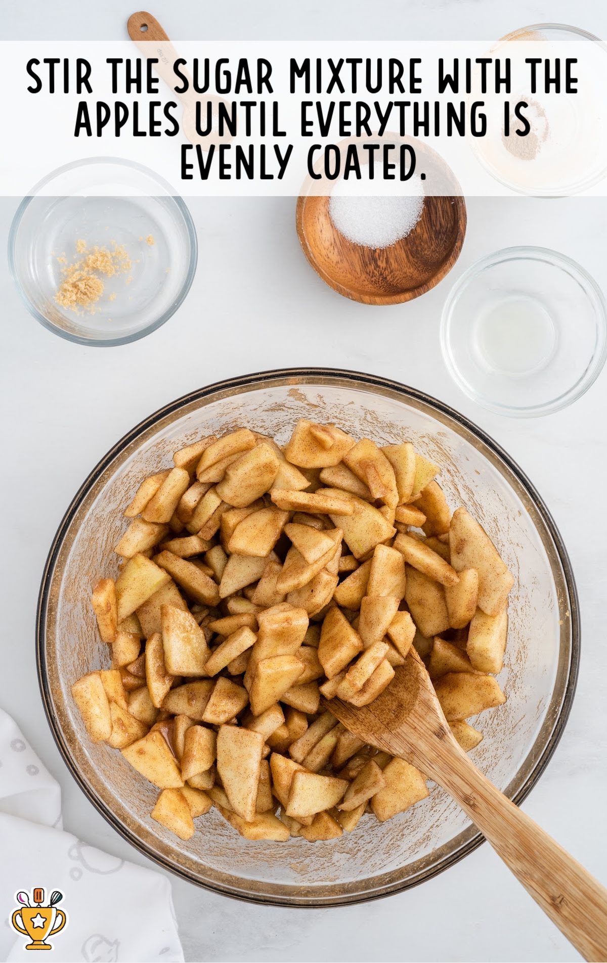 Apple slices in a mixing bowl with a wooden cooking spoon.