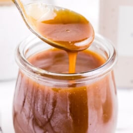 a small jar of caramel sauce with a spoon scooping out some of the sauce.