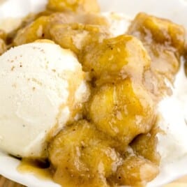 closeup of caramelized bananas in a white serving dish with a scoop of ice cream and a spoon