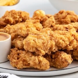 a white serving plate full of cooked chicken with dipping sauce.