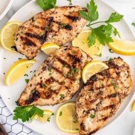 Greek Marinated chicken breast on a white plate with lemons to garnish.