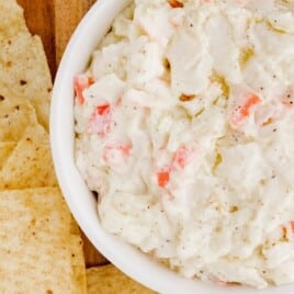 Imitation Crab Dip in a bowl on a wooden board with chips on the side