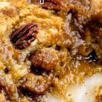 Close-up of a gooey pecan dump cake with a golden crust, visible toasted pecans, and a moist, caramelized filling in a glass baking dish. Text overlay reads “PECAN dump cake” and “EASY TO MAKE THANKSGIVING DESSERT!!” with a playful arrow pointing to the dessert.