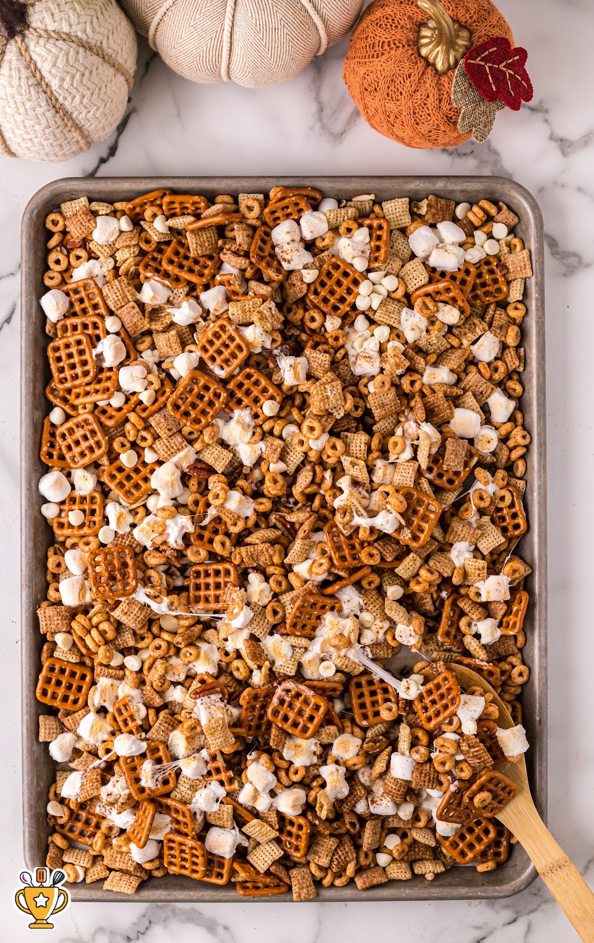 A baking pan with Pumpkin Spice Chex Mix with a wooden cooking spoon in it