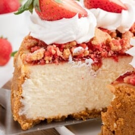 a cake lifter is lifting a slice of cheesecake out of the baked strawberry crunch cheesecake.