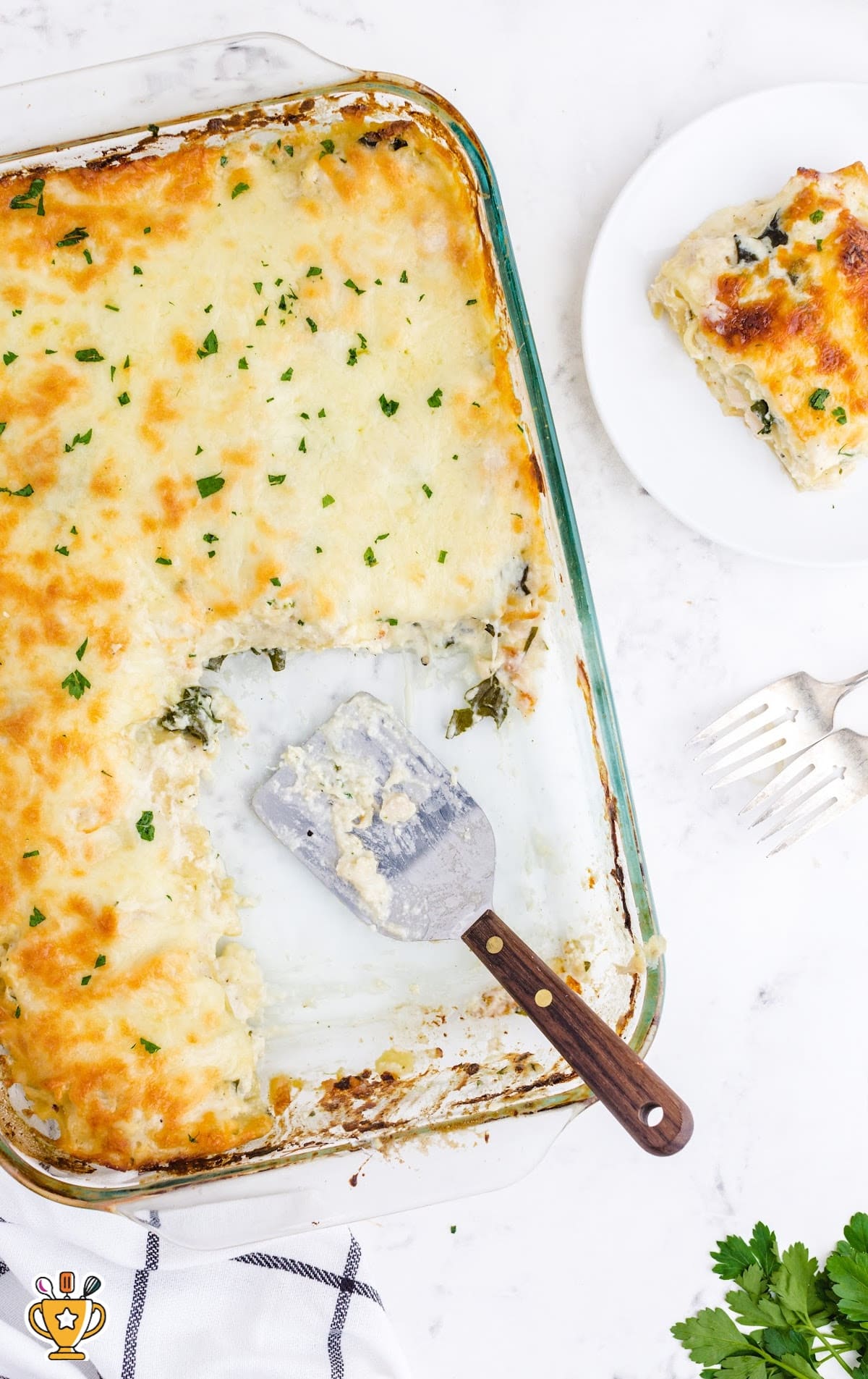 White Chicken Lasagna in a Glass baking pan with a spatula in the pan and a piece of Lasagna on a white plate on the side