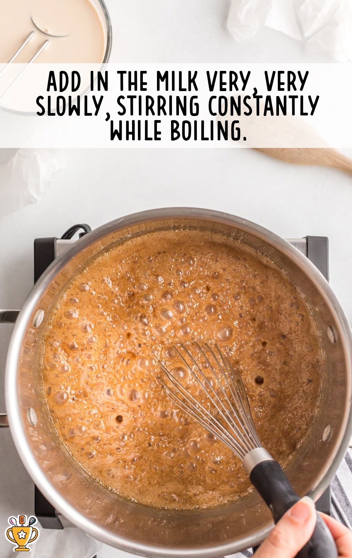 A pan containing the mixture for making Caramels with a hand holding a whisk mixing the mixture