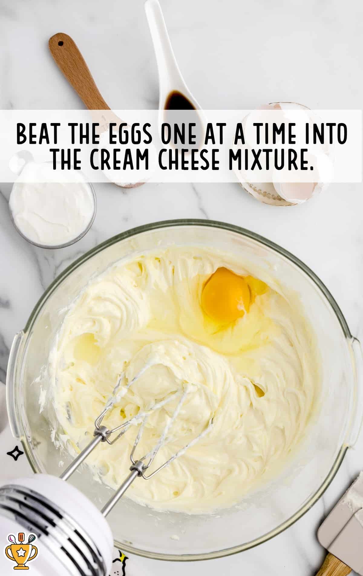 A Clear bowl containing cream cheese mixture and beaten eggs with a mixer in it