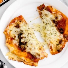 An air fryer pizza cut in half on a white plate.