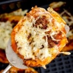 an air fried pizza being lifted out of the air fryer basket on a spatula.