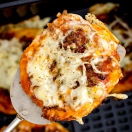 an air fried pizza being lifted out of the air fryer basket on a spatula.