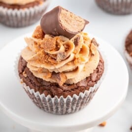 A Butterfinger Cupcake on a stand with a bunch of other Butterfinger Cupcakes surrounding it