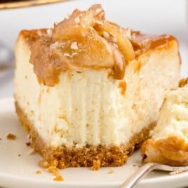 A piece of Caramel Apple Cheesecake on a plate with a fork holding a piece of cake