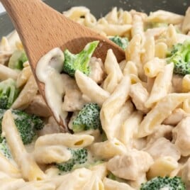 a skillet of pasta with a wooden spoon.