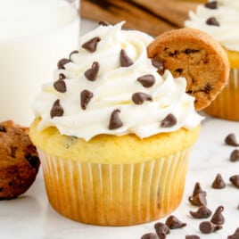 A chocolate chip cupcake next to a glass of milk.