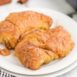 Two apple dumplings on a white dessert plate.