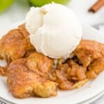 An apple dumpling with crescent rolls on a white plate with a scoop of ice cream.